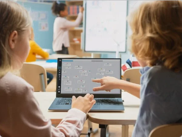 Dos alumnos siguen la sesión de Lumio desde su laptop mientras la maestra está en la pantalla