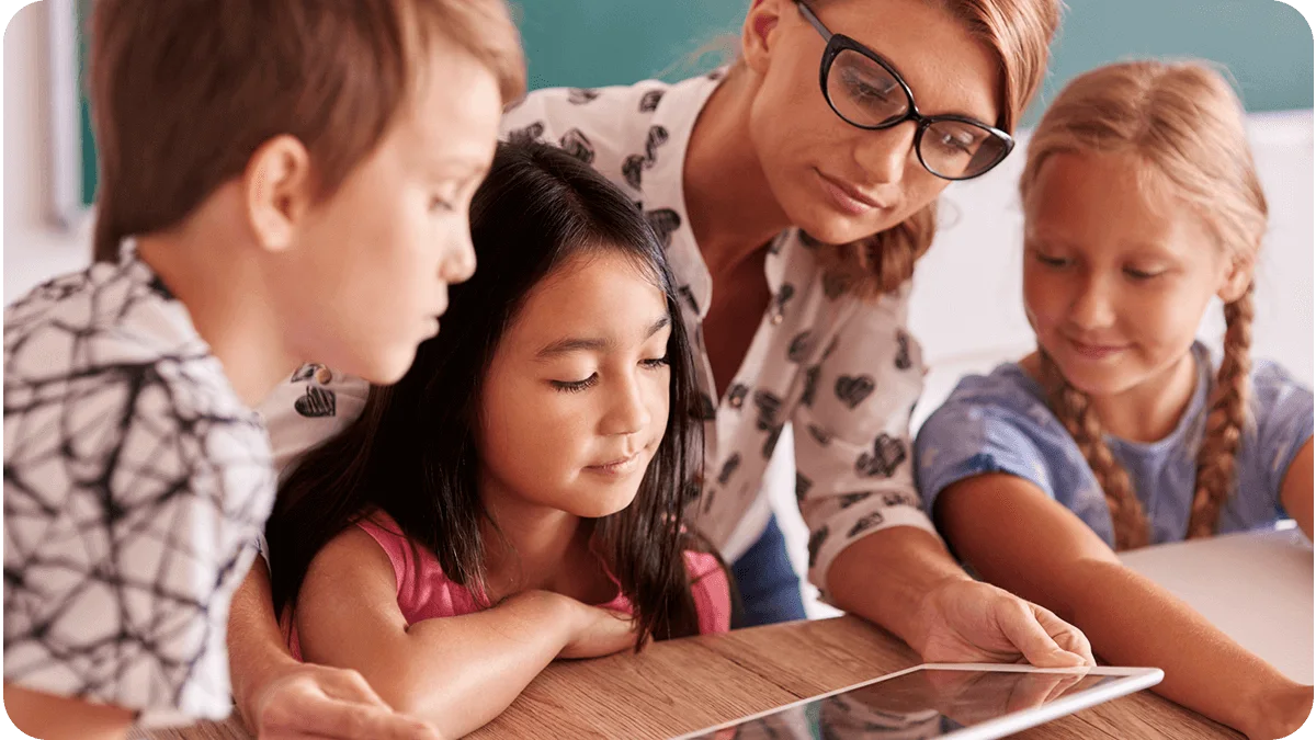 Maestra con tres alumnos revisando una actividad en una tableta
